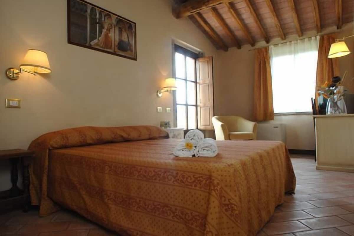 Una camera d'albergo con un letto, una sedia, una scrivania e un quadro appeso al muro.