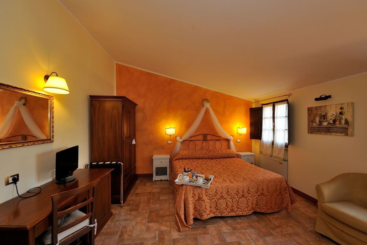 Una camera da letto con un letto a baldacchino, lampade ai lati del letto, un'armadio in legno, una televisione e una sedia.