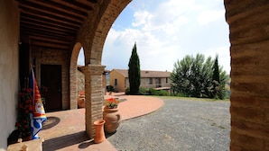 An outdoor courtyard with a stone archway, a tiled pathway, and a view of a building in the background. - Agrihotel Il Palagetto (Volterra)