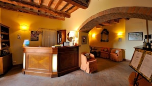 A cozy interior with a wooden reception desk, seating area, and exposed brick arches. - Agrihotel Il Palagetto (Volterra)