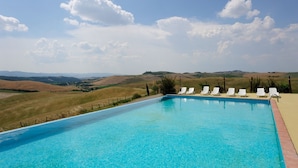 A swimming pool with white lounge chairs and a view of rolling hills. - Agrihotel Il Palagetto (Volterra)