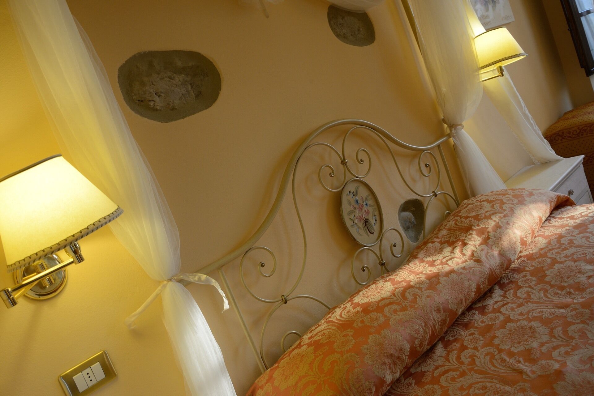 A bed with a metal headboard, two wall-mounted lamps, and a power outlet.