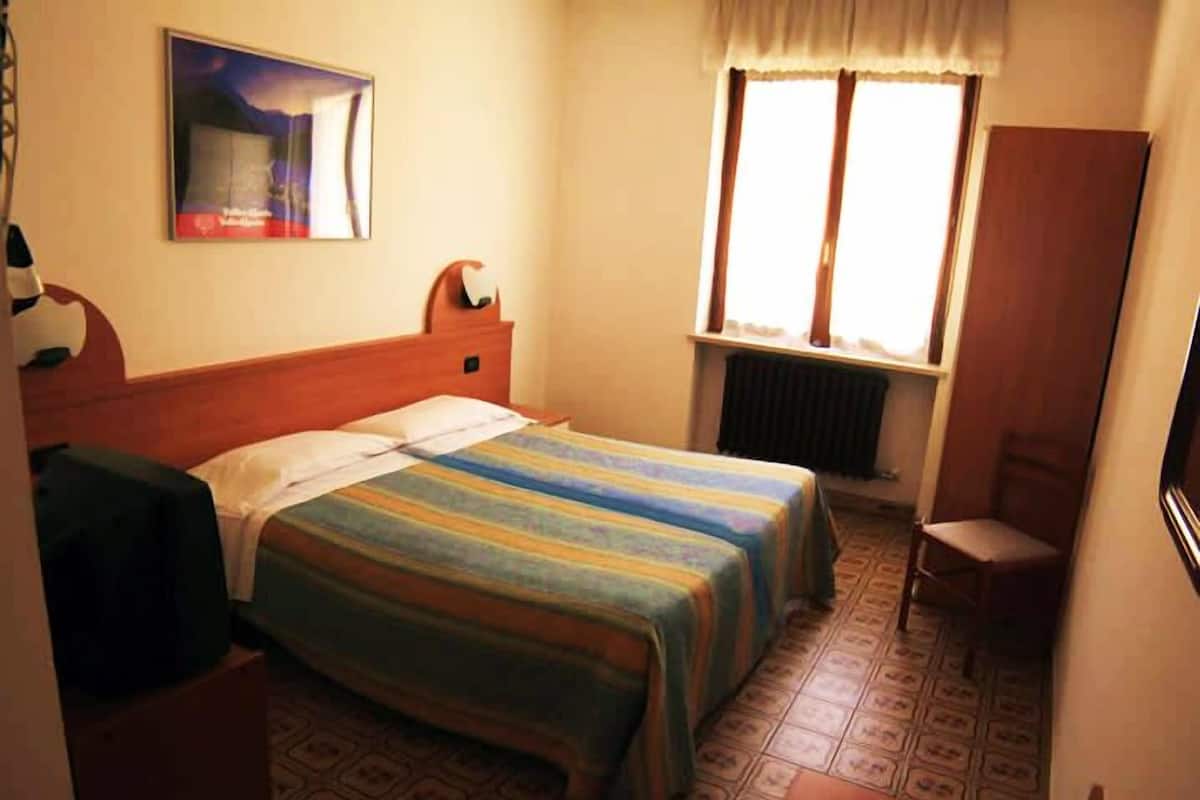 A bedroom with a bed, a chair, a radiator, and a window with curtains.