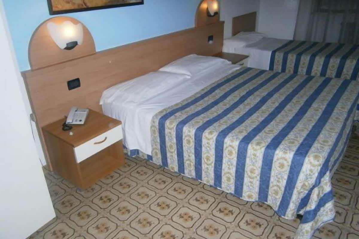 A hotel room with two beds, a wooden headboard, a bedside table with a phone, and patterned carpet.