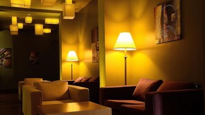 A warmly lit lounge area with sofas and a coffee table, featuring artwork on the walls and pendant lighting. - Mosaic City Hotel (Madaba)