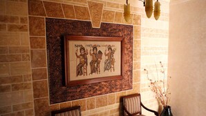 A framed artwork on a stone wall, two upholstered chairs, and a vase with dried plants. - Mosaic City Hotel (Madaba)