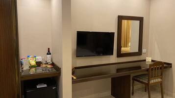 Een hotelkamer met een bureau, stoel, televisie, minibar en een prullenbak.