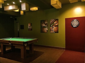 Una mesa de billar en una habitación con poca luz, paredes verdes, un dardo y arte abstracto.