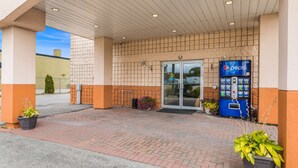 A building entrance with a Pepsi vending machine, potted plants, and a covered walkway. - Knights Inn Orillia (Orillia)