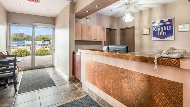 A hotel reception area with a counter, a phone, and a sign for Knights Inn. - Knights Inn Orillia (Orillia)