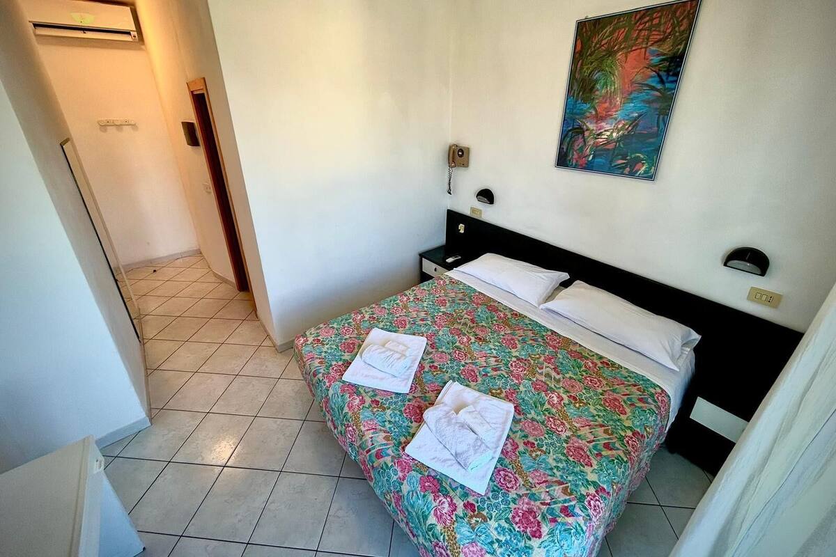 A hotel room with a bed, a nightstand, a telephone, and a painting on the wall.