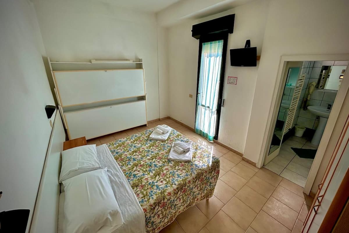 A small, simple room with a bed, a wardrobe, and a bathroom visible through an open door.