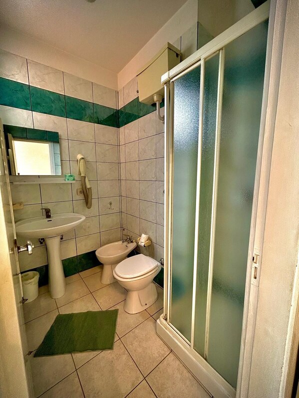 A bathroom with a sink, two toilets, a mirror, and a shower with frosted glass doors. - Hotel Sacramora (Rimini)