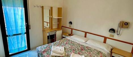 A bedroom with a bed, a desk, a chair, a telephone, and a window with curtains.