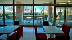A restaurant with large windows, outdoor seating, and a view of the beach. - Hotel Sacramora (Rimini)
