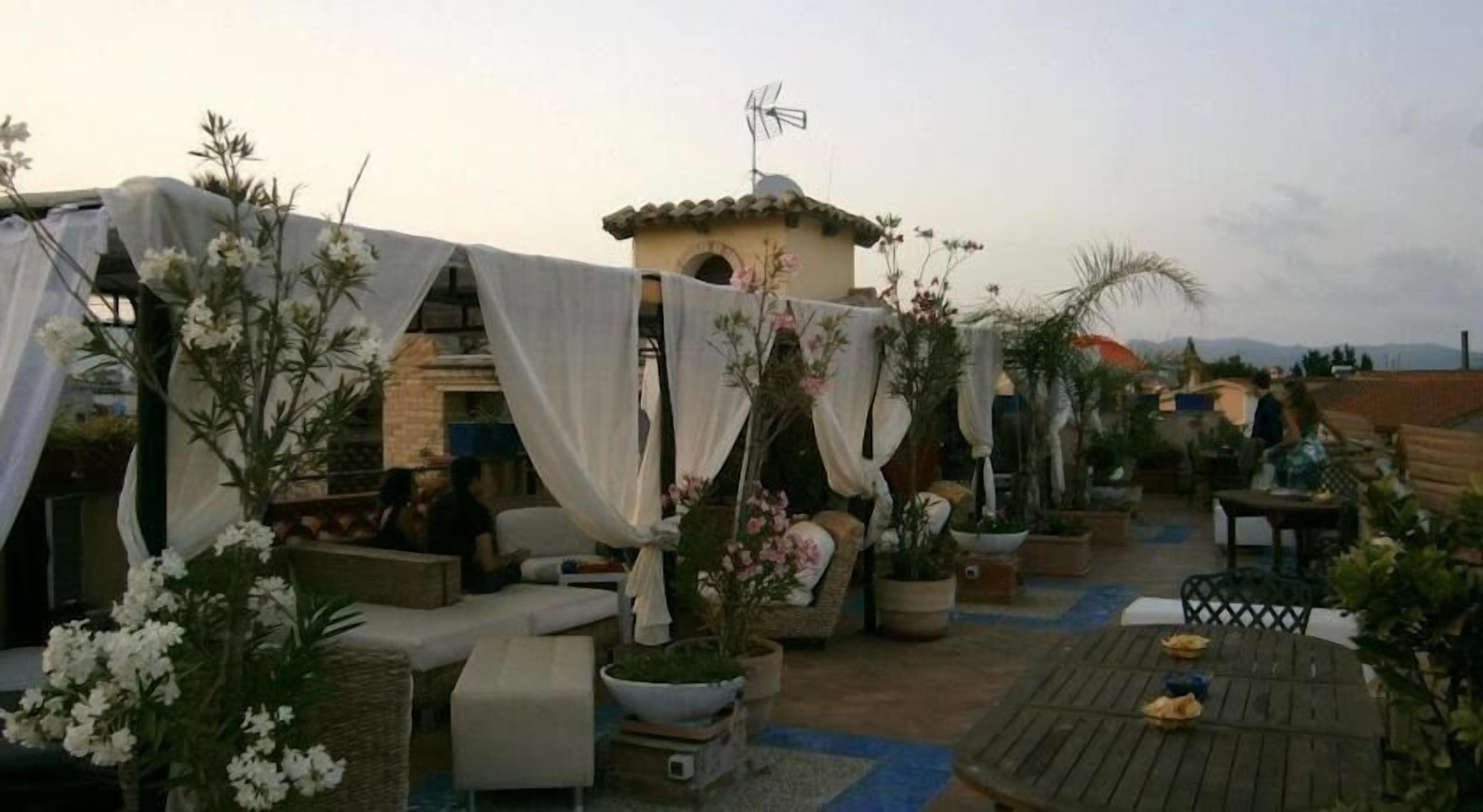 Un patio al aire libre con arreglos de asientos, plantas en macetas y un edificio pequeño con antena parabólica.