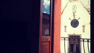 Vista desde un balcón con puerta de madera y barandilla de metal, que da a un edificio con un reloj y un ventanal circular.