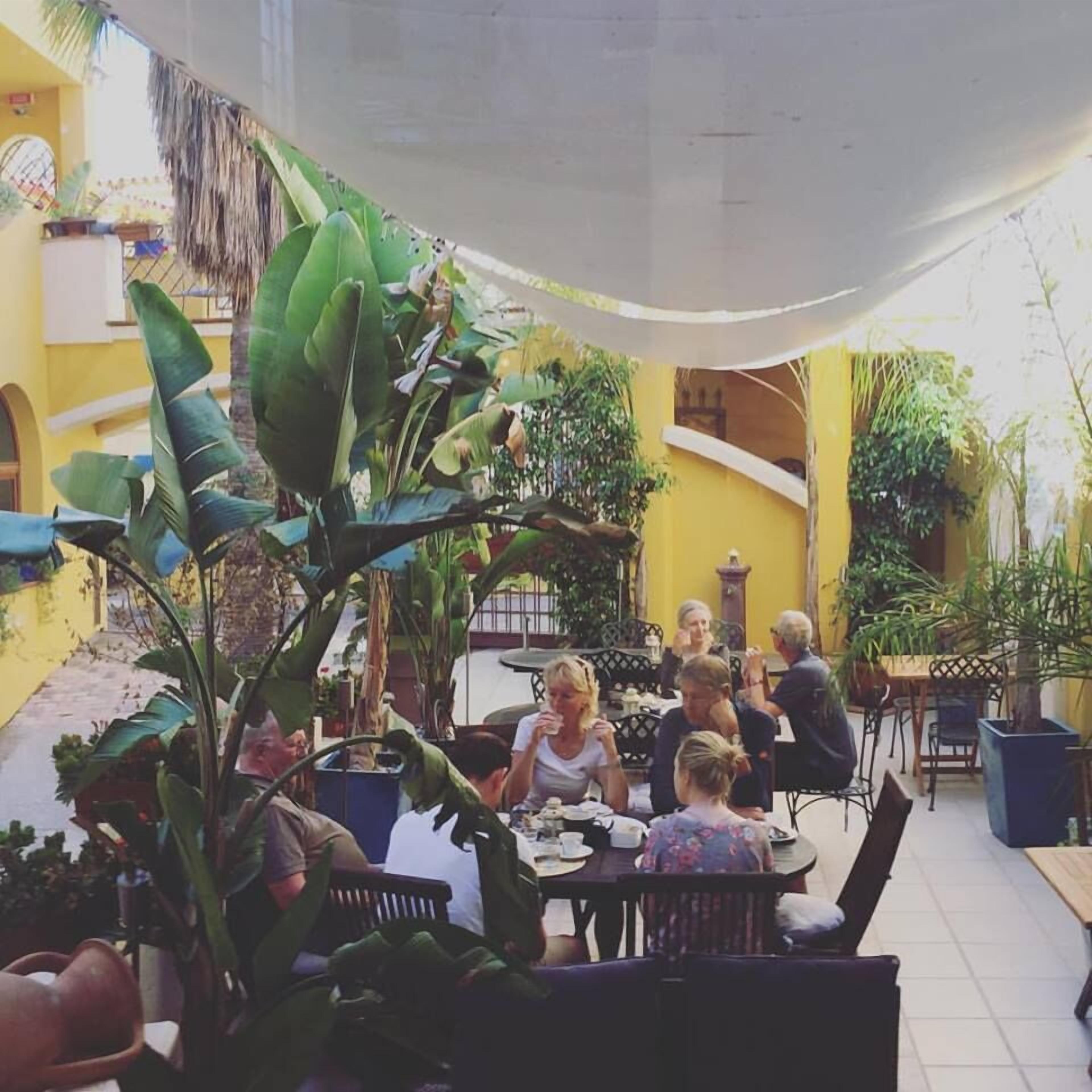 An outdoor dining area with yellow walls, potted plants, and a thatched roof.