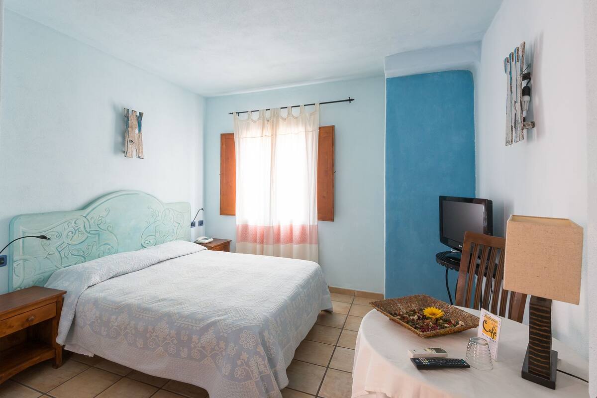 A bedroom with a bed, a nightstand, a TV, a table with a lamp, and a decorative tray.