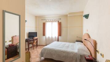Habitación de hotel con cama, escritorio con computadora, silla, teléfono y espejo.