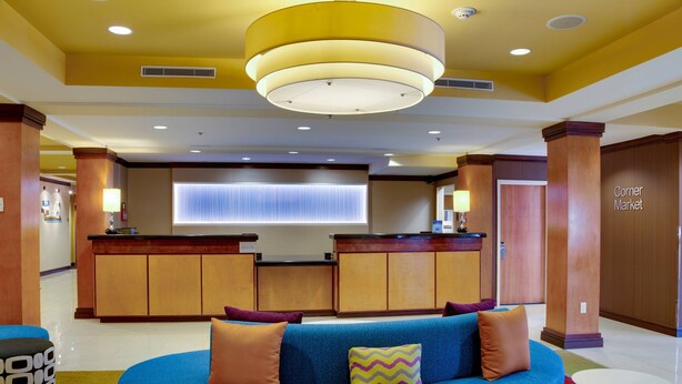 A hotel lobby with a blue sofa, a reception desk, and a 'Corner Market' sign. - Fairfield by Marriott Titusville Kennedy Space Center (Titusville)