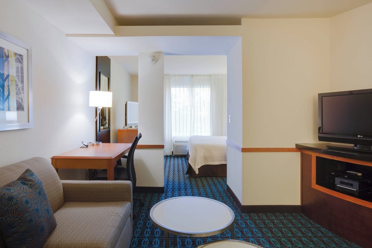 Une chambre d’hôtel avec un lit, un bureau doté d’une lampe, une télévision et une moquette à motifs.