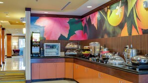 A hotel buffet area with a colorful mural, a self-service beverage machine, and a variety of food items displayed. - Fairfield by Marriott Titusville Kennedy Space Center (Titusville)