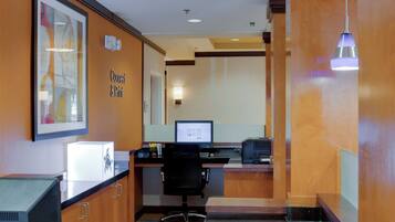 A hotel reception area with a desk, computer, and a framed artwork on the wall.