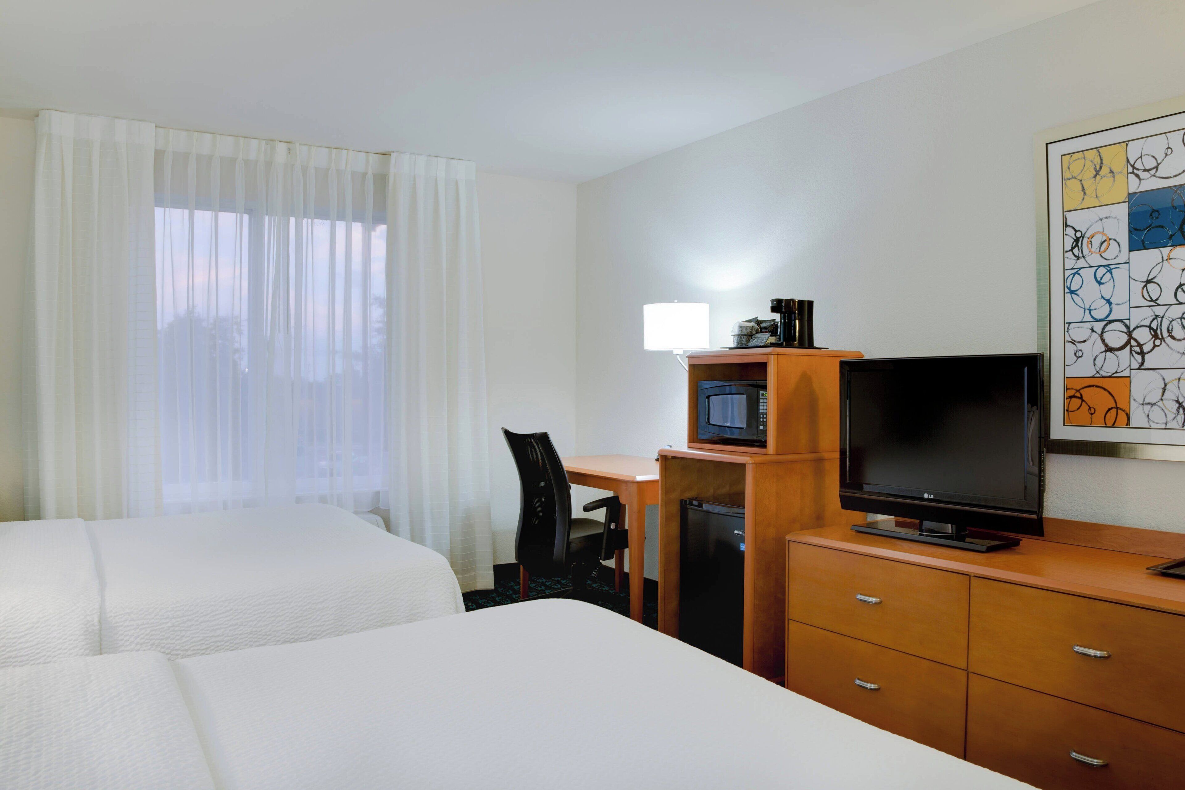 A hotel room with two beds, a desk with a television, a microwave, and a coffee maker.