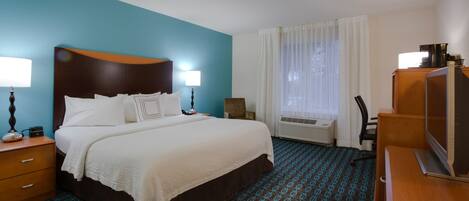 A hotel room with a large bed, a desk, a chair, and a television.