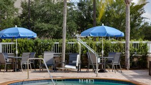 A pool area with lounge chairs and umbrellas, surrounded by greenery. - Fairfield by Marriott Titusville Kennedy Space Center (Titusville)