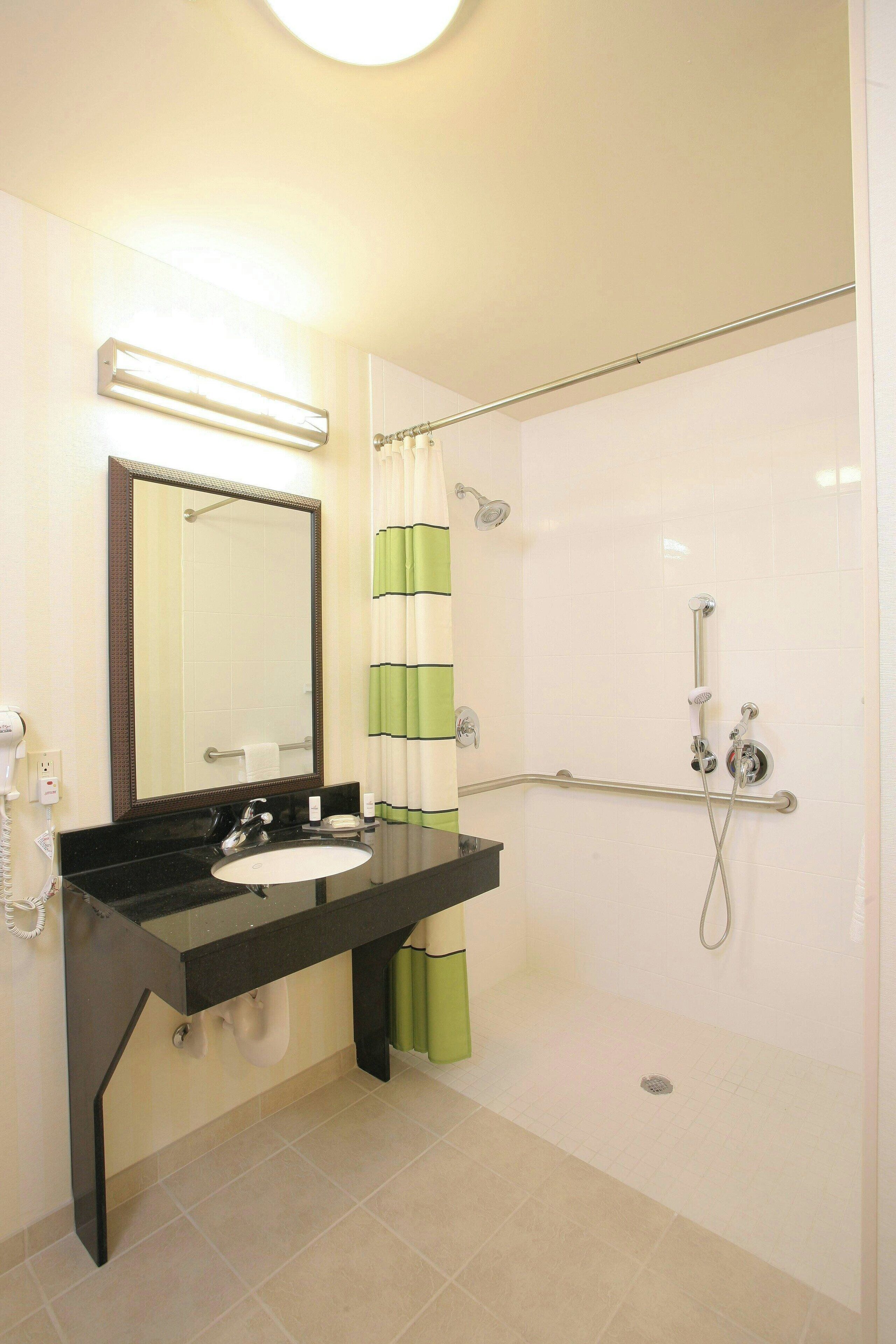 A bathroom with a black sink, a mirror, a shower with a grab bar, and a green and white striped shower curtain.