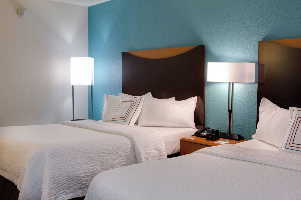 Une chambre d’hôtel avec deux lits, une table de chevet et une lampe.