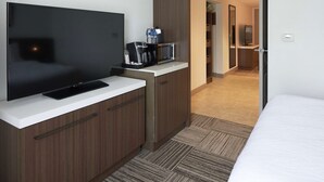 Habitación de hotel con televisión de pantalla plana, cafetera y microondas sobre una encimera.