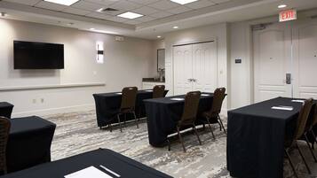A conference room with tables, chairs, a flat-screen TV, and an exit sign.