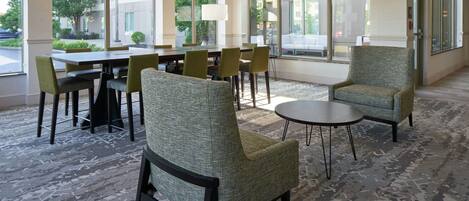 A spacious hotel lobby with large windows, a modern chandelier, and comfortable seating areas.