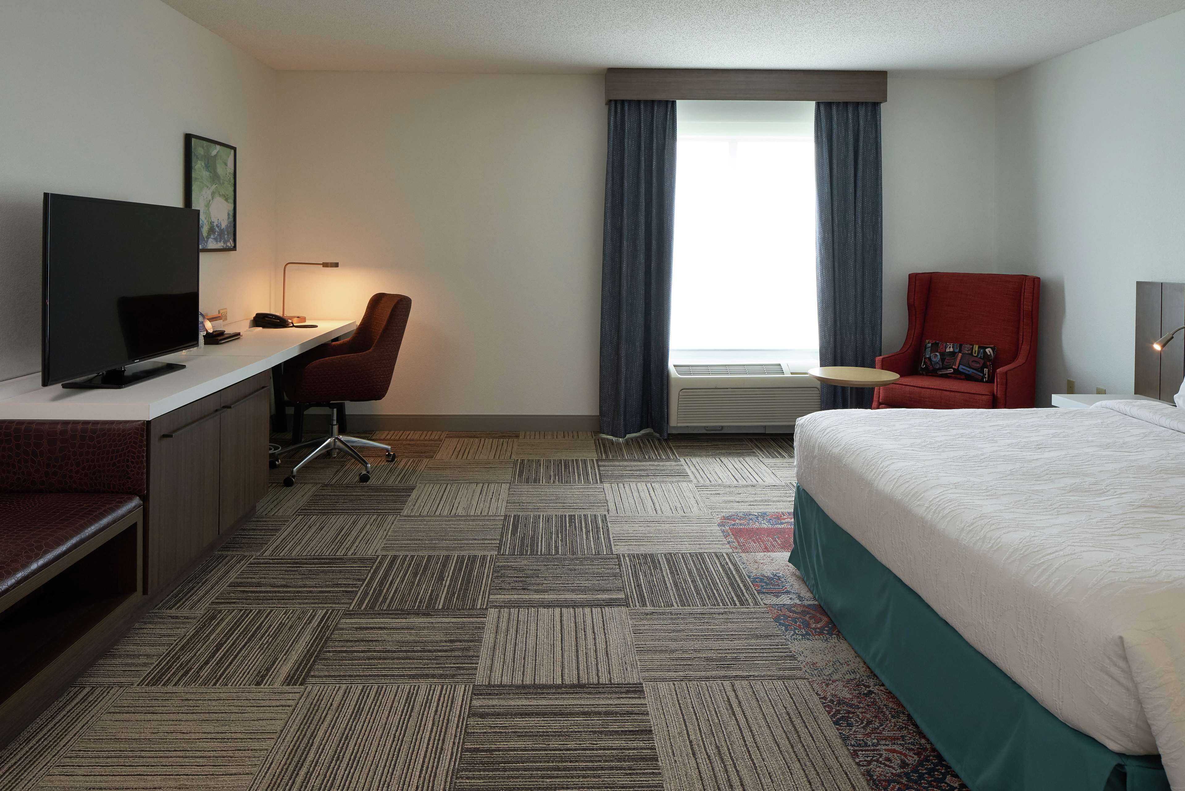 A hotel room with a bed, desk, chair, television, and a window with curtains.