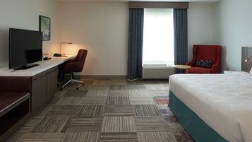 A hotel room with a bed, desk, chair, television, and a window with curtains.