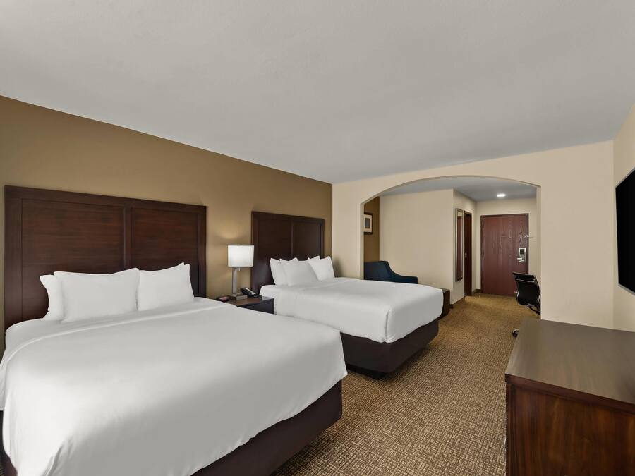 Habitación de hotel con dos camas, un escritorio, un televisor y una puerta que da a otra habitación.