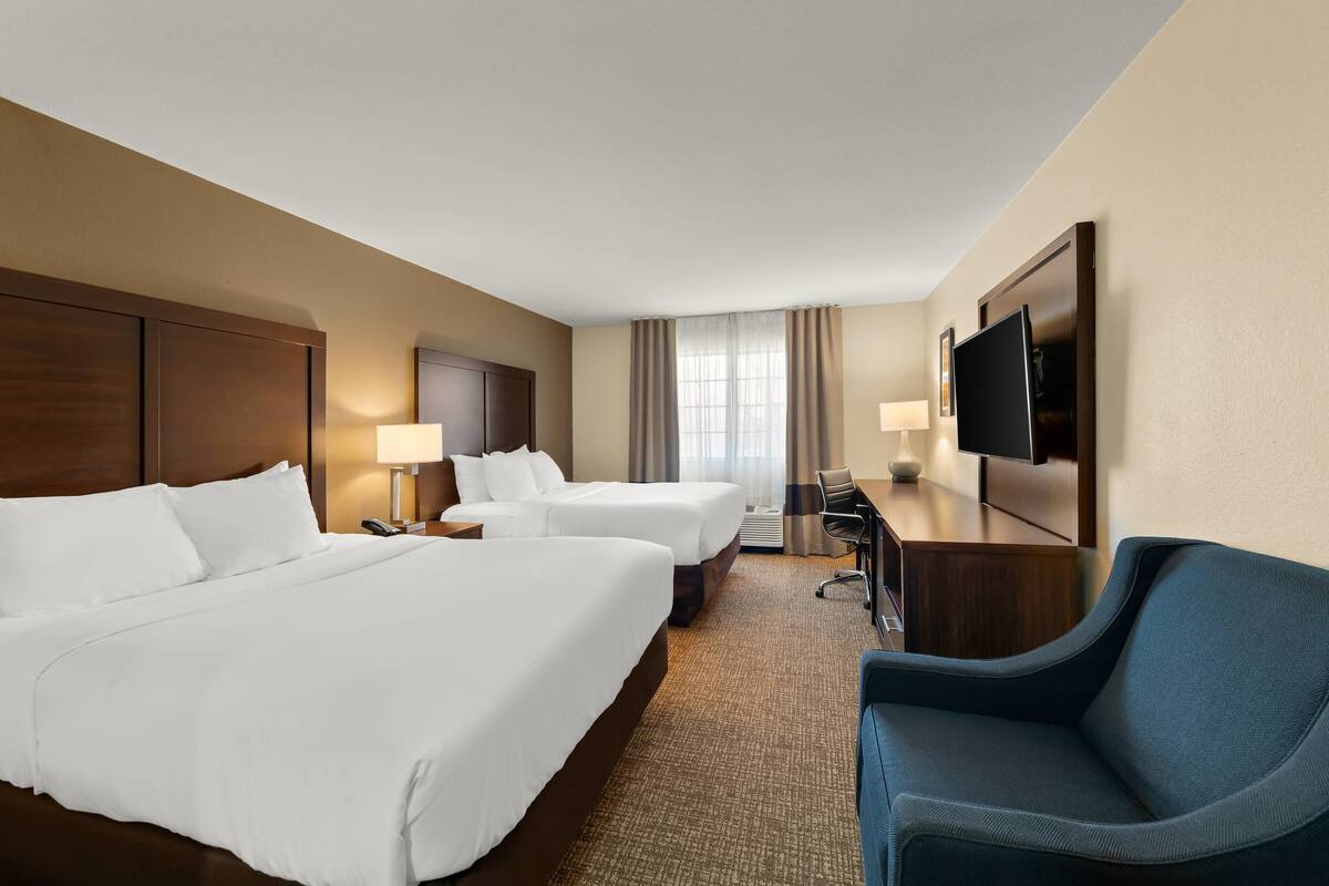 A hotel room with two beds, a desk, a chair, a TV, and a window with curtains.