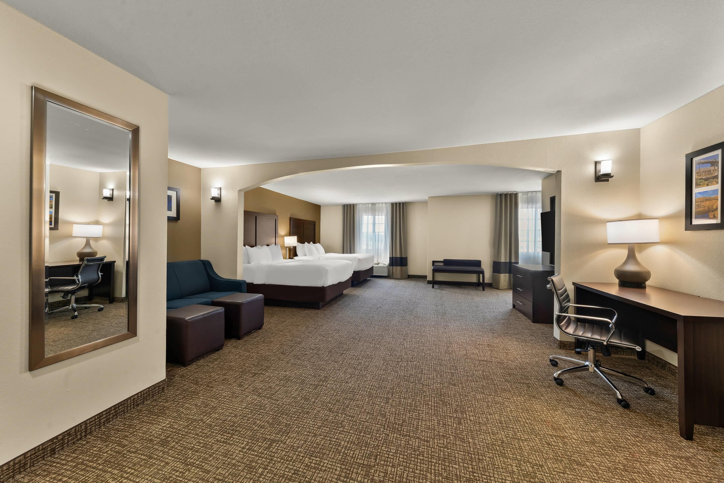 A hotel room with a large bed, a desk, a chair, a sofa, and a mirror.