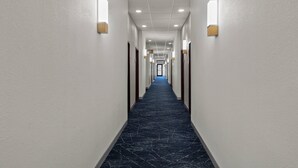 A long, narrow hotel corridor with white walls, dark marble flooring, and recessed lighting.