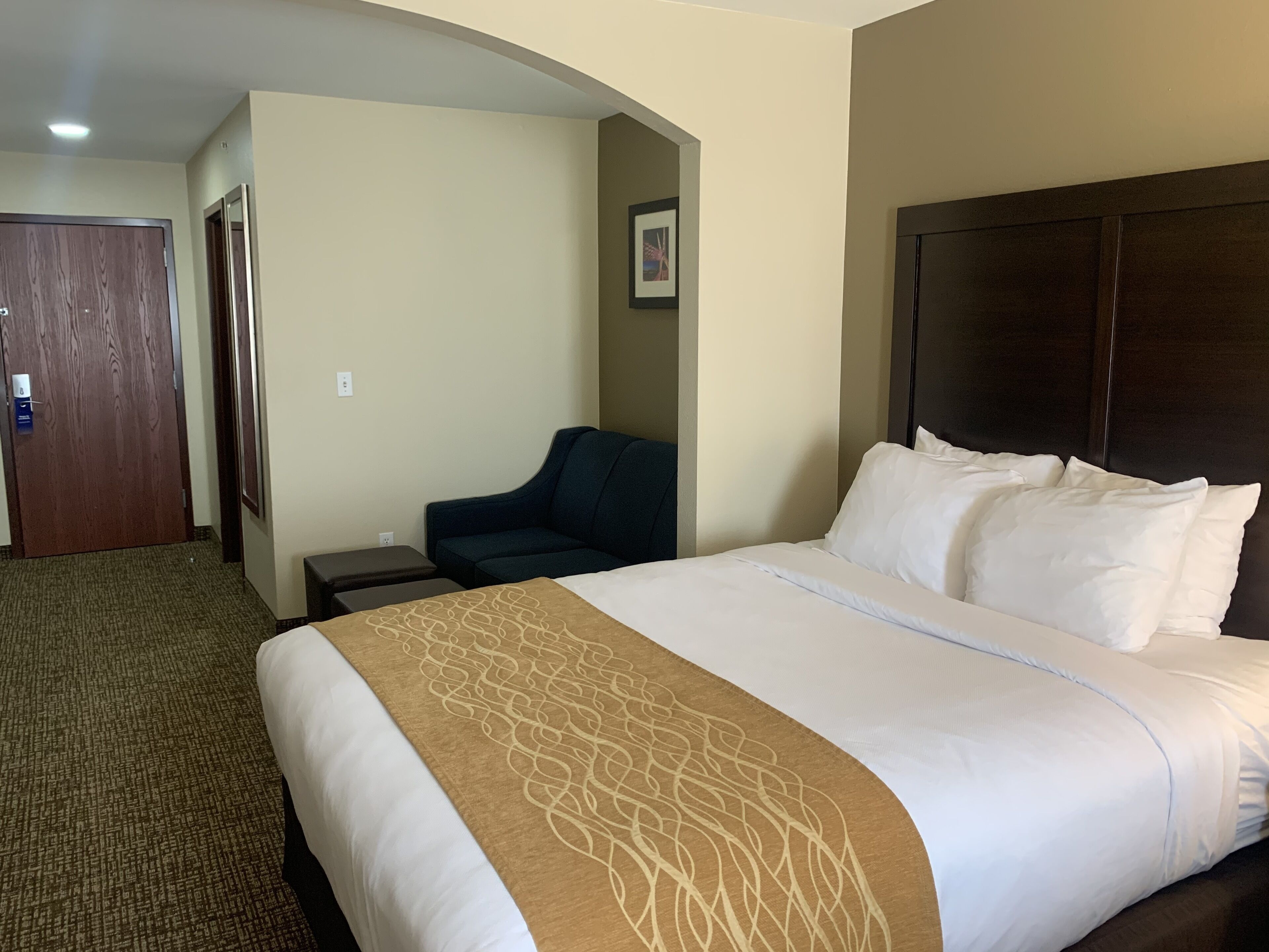 A hotel room with a large bed, a dark headboard, a small desk, a chair, and a door.