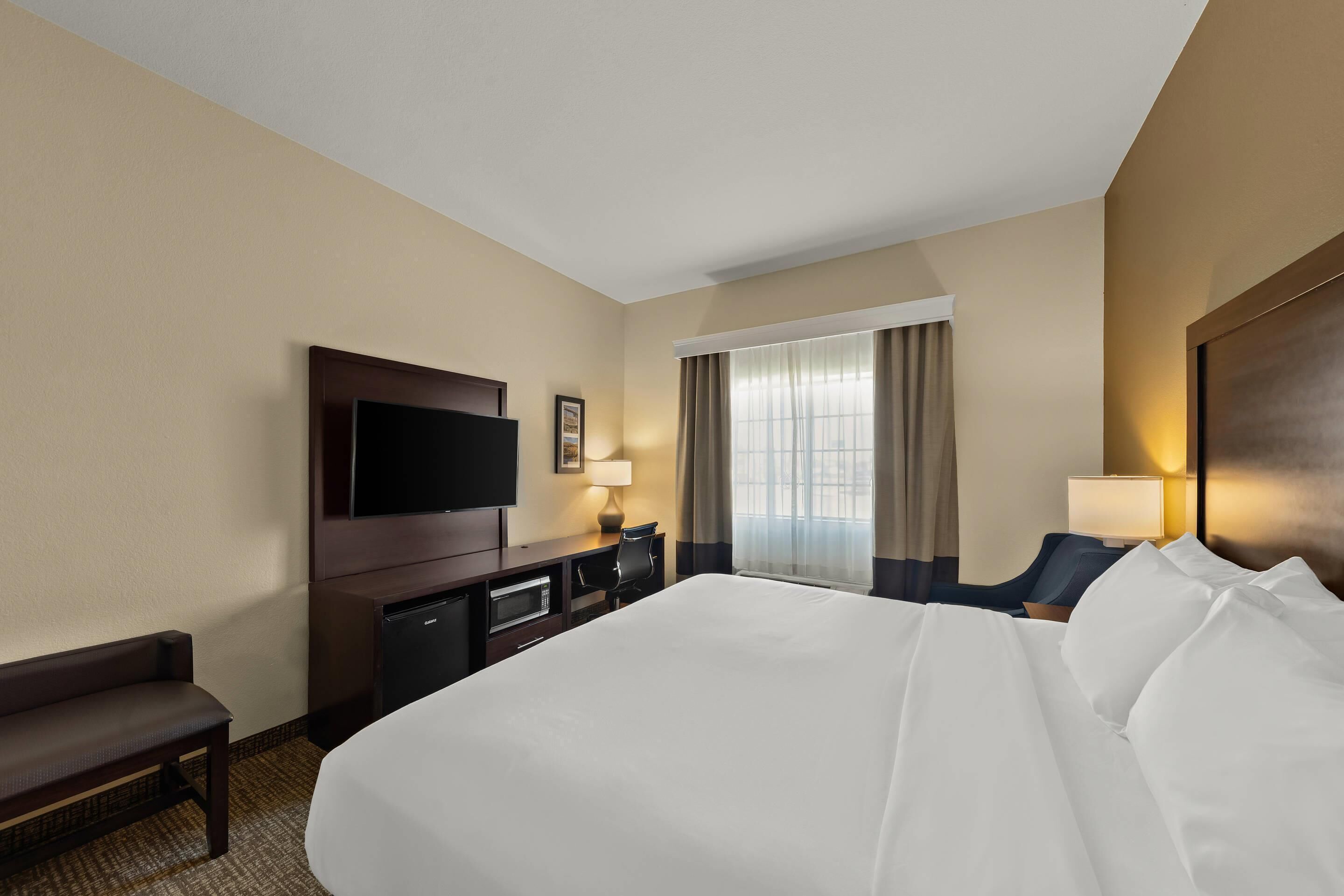 Quarto de hotel com uma cama grande, televisão, escrivaninha com cadeira e janela com cortinas.
