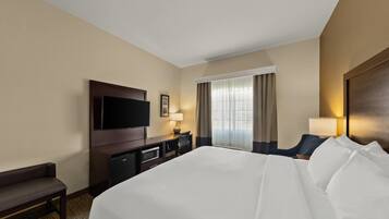 Quarto de hotel com uma cama grande, televisão, escrivaninha com cadeira e janela com cortinas.