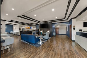 A modern hotel lobby with a reception desk, seating area, and a bar.