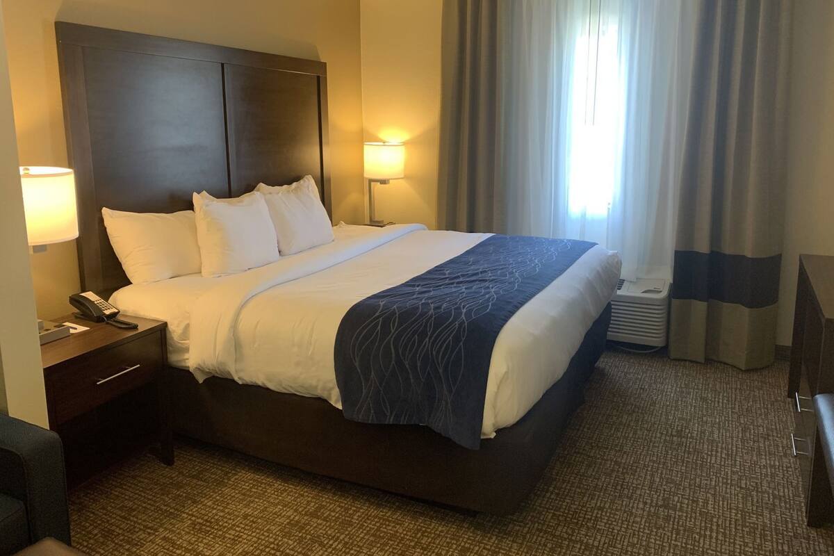 A hotel room with a large bed, bedside lamps, a telephone, a desk, and a window with curtains.