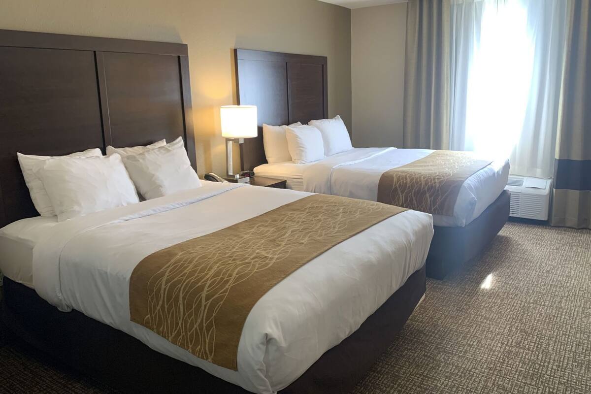 Two double beds with headboards, a bedside table with a lamp, and a window with curtains.