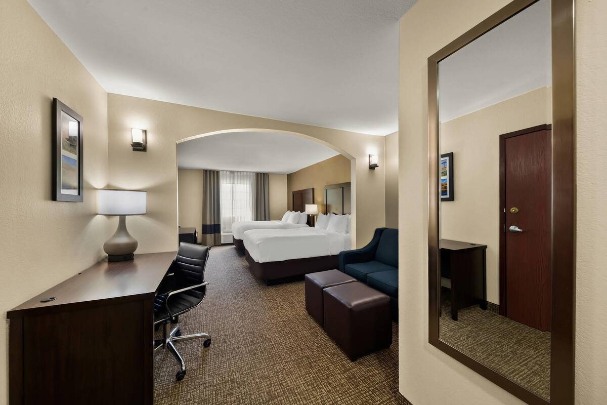 A hotel room with a desk, two beds, a sofa, a mirror, and a door.
