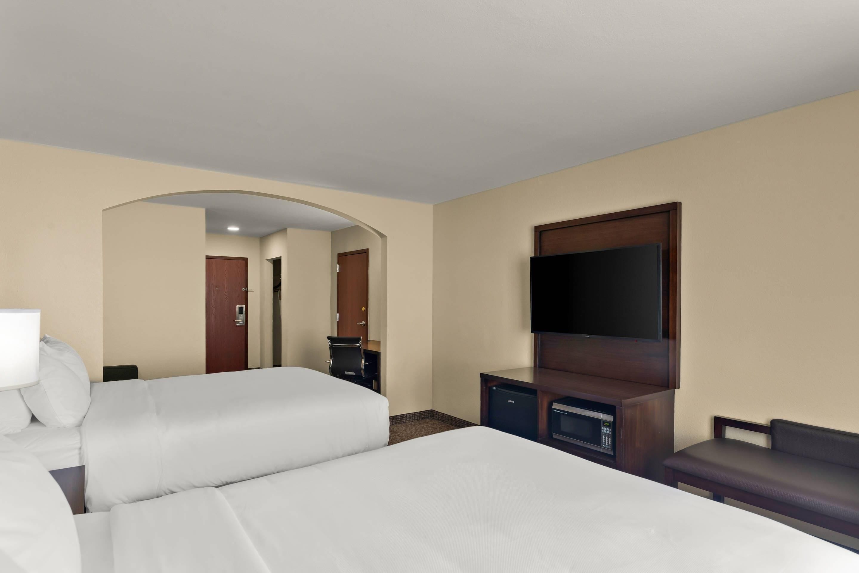 A hotel room with two beds, a TV, a desk, and a small seating area.